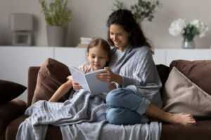 mother and child snuggle under blanket on couch while reading