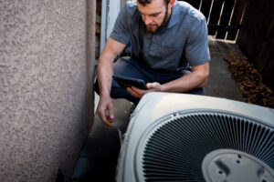 Technician inspecting line to a Residential Air Conditioner Condenser Unit at the side of a stucco home